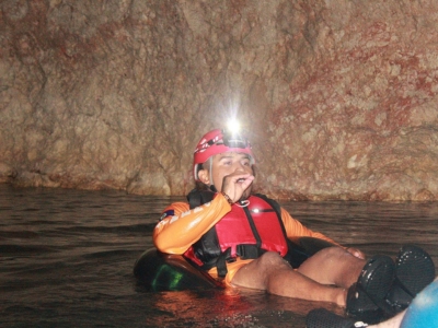 A professional tour guide in a safety helmet and life vest leads a cave tubing tour through an ancient cavern near Hopkins and Placencia, Belize.