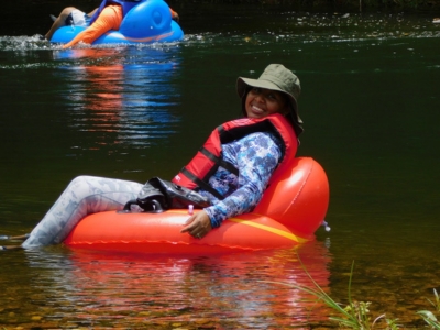 A happy woman with a life vest and hat floats on an orange river tube during a tour near Hopkins and Placencia, Belize.