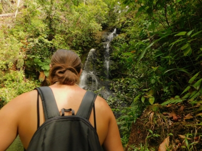 A hiker with a backpack views a scenic jungle waterfall during a guided tour near Placencia and Hopkins, Belize.